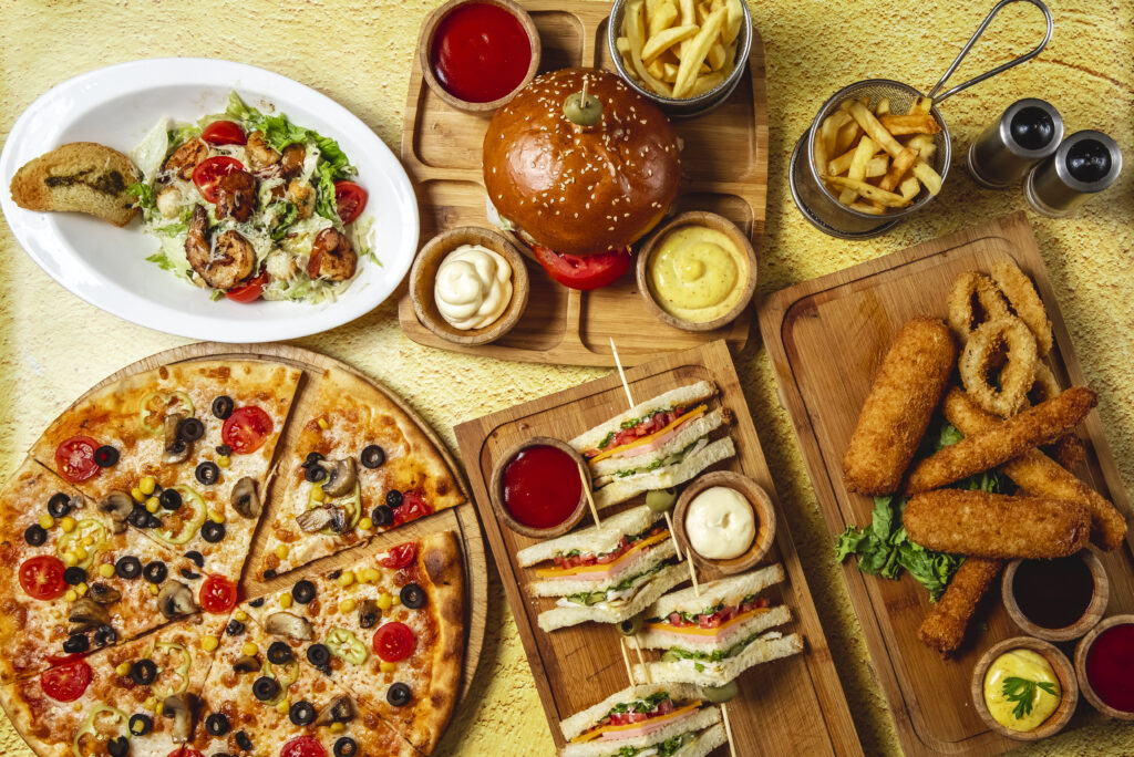 top view fast food mix mozzarella sticks club sandwich hamburger mushroom pizza caesar shrimp salad french fries ketchup mayo and cheese sauces on the table